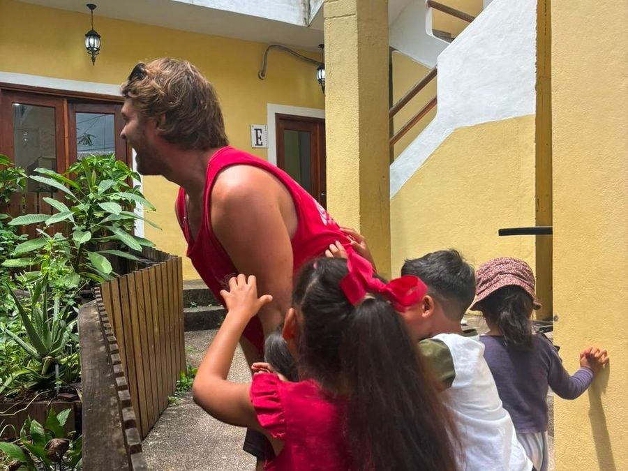 Ian, in profile, with four children reaching up and gathered around him in a courtyard.