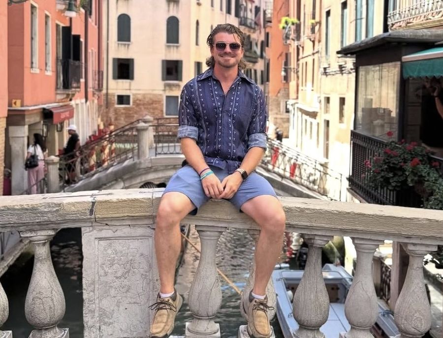 Ian Treger sitting on a stone bridge railing over a canal in Venice.