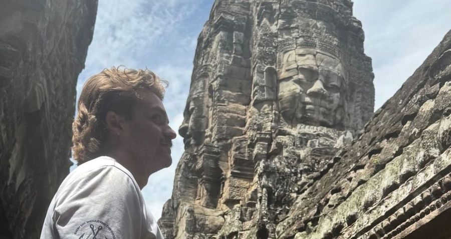 Ian Treger looking up at a carved stone face on a tower at Angkor Thom, Cambodia.