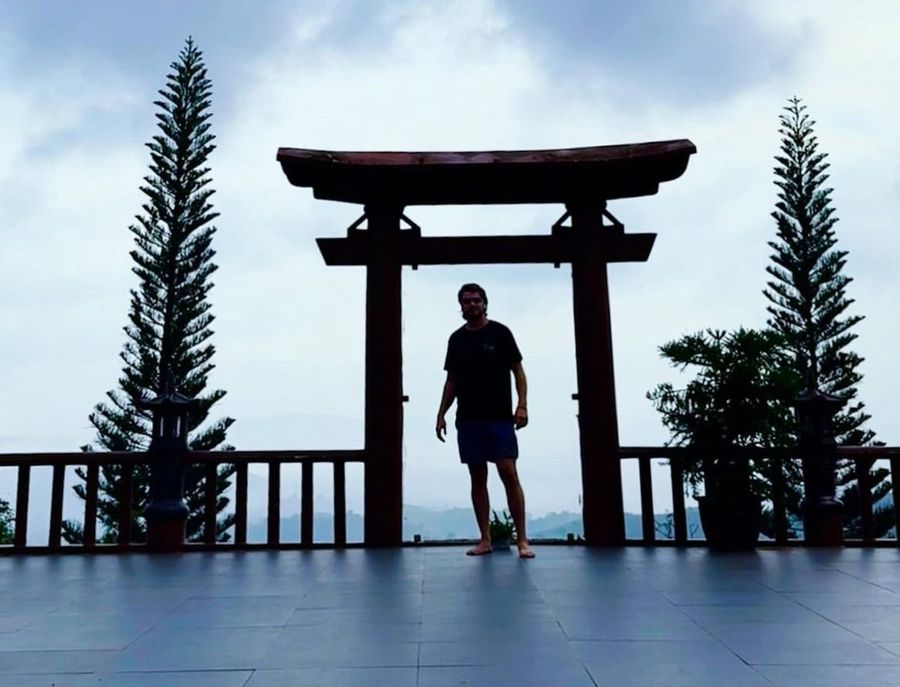 Ian silhouetted beneath a torii gate at dusk, in Asia.