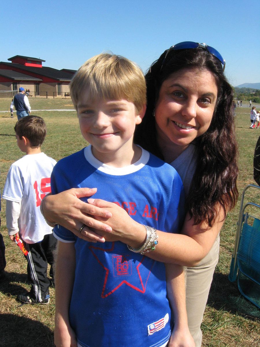 Ian as a young boy in a blue soccer jersey, held in a hug by his aunt Celine at the side of a playing field.