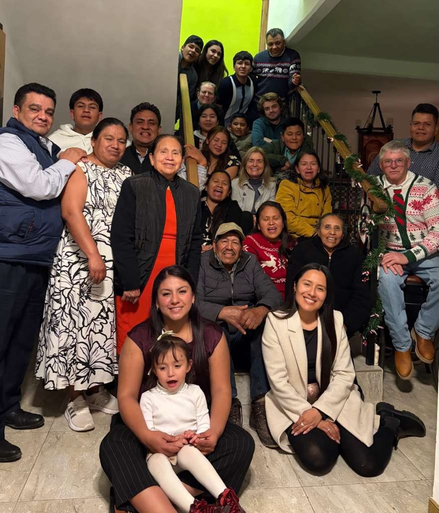 Ian's extended family and close friends in Mexico, more than twenty people of all ages posed together on a staircase decorated with holiday garland.