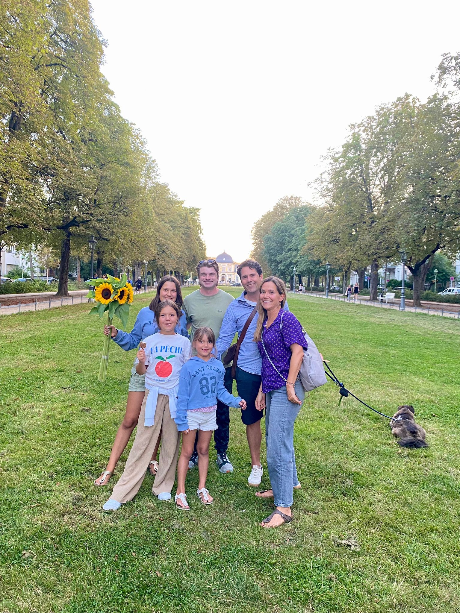 Ian, sunglasses pushed up into his hair, standing with his German host family &mdash; two parents, three children and their small dog on a leash &mdash; on a grassy, tree-lined boulevard, one holding a bunch of sunflowers.