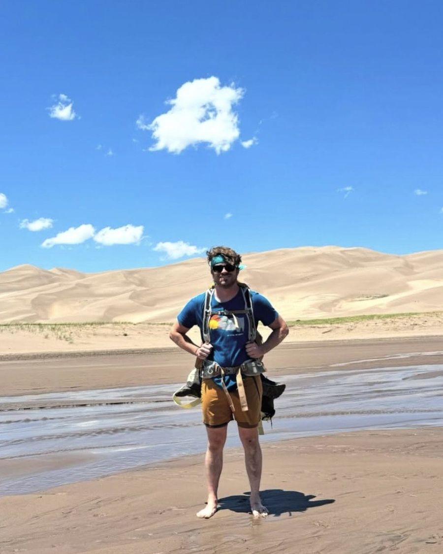 Ian Treger standing on a wide sandbar with sand dunes rising behind him.
