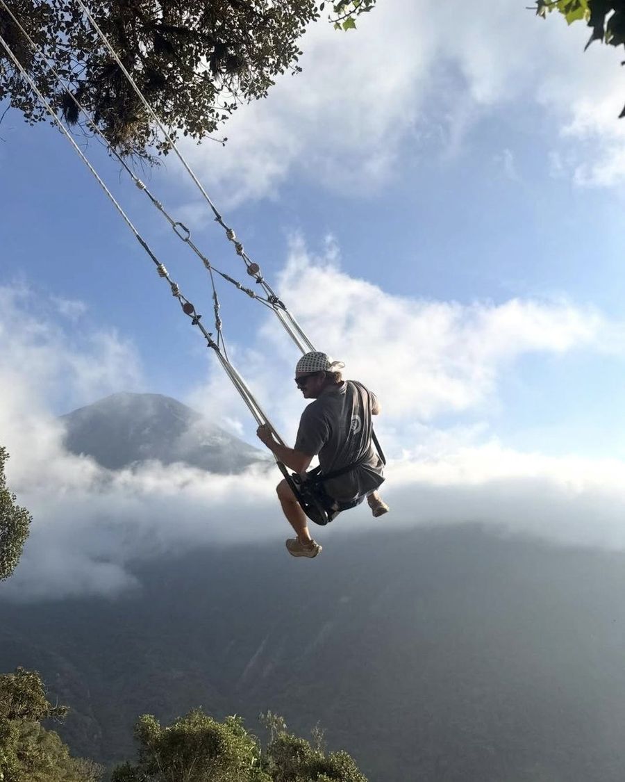 Ian Treger riding a rope swing out over a cloud-filled valley, a mountain rising through the cloud behind him.