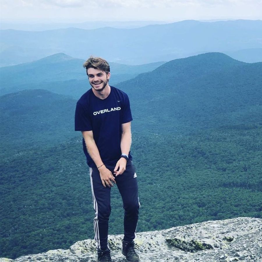 Ian Treger standing and laughing on a bare summit, wooded ridges behind him.