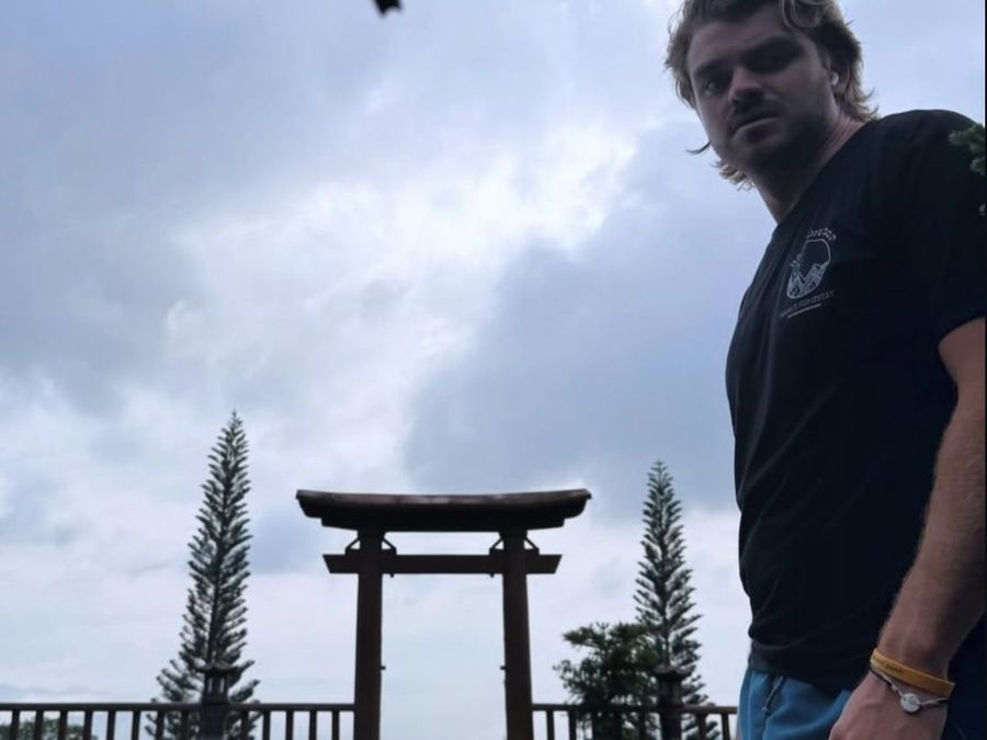 Ian Treger beside a torii gate on an overlook, pine trees and cloud behind him.