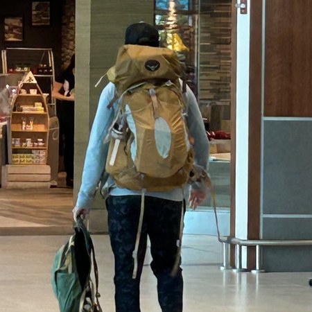 Ian walking through an airport terminal, wearing a full hiking pack and carrying a duffel bag.